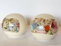 Two Bunnykins round money banks side by side showing illustrated scenes and coin slots