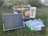 Lite-Brite unit, box, and bags of pegs displayed on grass