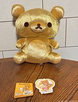 Front view of gold Rilakkuma plush bear with two hang tags displayed