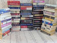 Wide view showing several tall stacks of pocket paperbacks arranged on floor, various titles and authors visible
