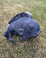 Left side view of resin koi fish statue on grass showing scale texture and overall form