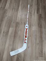 Full view of white ITECH composite goalie stick on wood floor