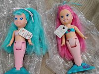 Front view of both mermaid dolls showing hair colors, tails, stands