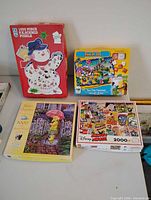 Four puzzle boxes displayed: FX Schmid snowman 1000 pc, Puzzle Doubles Find It 123 50 pc, SeedOut Better Together 1000 pc, Disney Mickey Mouse collage 2000 pc