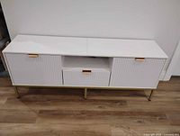 Front view of white TV stand showing doors, drawer, gold base