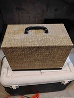 Closed beige tweed-style carrying case with black handle