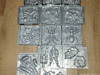 Thirteen metal molds laid out in rows showing insect and Marvel designs