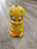 Front view of yellow Tweety Bird coin bank standing on wood floor