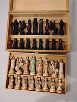 Open wooden box showing complete set of 32 light and dark hand-painted chess pieces in fitted trays