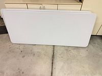 Two white plastic tables standing on edge showing tops