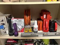 Shelf view of assorted tools including flashlights, extension cord reel, spade bits, cutting oil, bench vise parts, level
