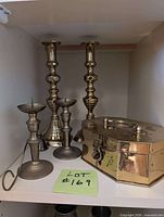 Four brass candlesticks and brass trinket box grouped on shelf