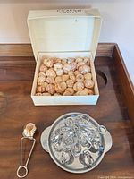 Open box of escargot shells beside tray filled with tongs and holders