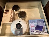 Drawer view of all items: salad spinner lid, boxed SouperStrain, two grinders, boxed Sila sanitizer