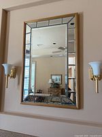 Full view of the framed rectangular wall mirror mounted on wall between sconces