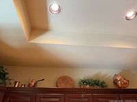 Overview of all items atop cabinet: teapot, creamers, tray, faux plant, colanders