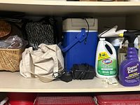 Shelf showing wicker basket, canvas tote, zebra-print bag, blue cooler with adapter, assorted cleaner bottles
