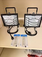 Two Regent portable halogen work lights with cords and two packaged 150W bulbs