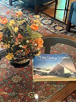 Silk floral arrangement in ceramic bowl on wooden stand beside book