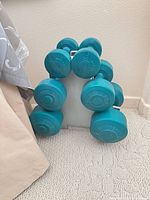 Front view of all six teal dumbbells on white rack