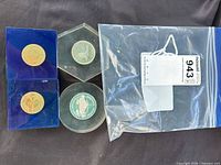 Overview of four lucite blocks with coins and labelled bag