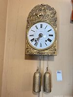 Full view of clock on wall showing brass front, dial, weights