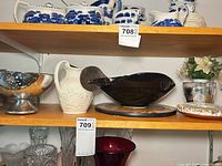 Shelf view showing silver-tone compote, white embossed pitcher, partial black dish unrelated