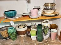 Overall view of top and bottom shelves showing variety of bowls, plates, pink tumblers and stacked metal bowls