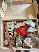 Open box showing red marbled teapot and wrapped saucer plus packing