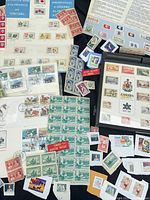 Overview of assorted Canadian and U.S. stamps including full sheets, blocks, album pages and FDCs spread on table