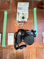 Both Canon cameras, manual, strap and lens cap arranged on tiled surface