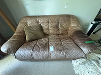 Front view of brown/tan leather loveseat with pillow