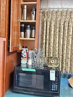 Microwave on counter beneath cabinet containing several stainless travel mugs and mixer attachments