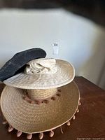 Stack of three hats showing straw sombrero with tassels, beige sun hat, black winter hat