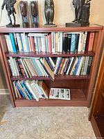Front view of reddish-brown three-shelf bookcase filled with books (books not included)