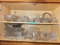 Wide shot of entire cabinet shelf showing majority of pressed glass pieces and silver accent items