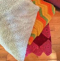 Stack showing shaggy throw, chevron crochet afghan and pink granny-square afghan