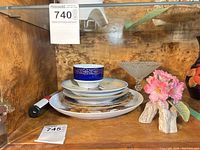 Shelf view showing stack of plates, cobalt cup, glass compote and floral figurine