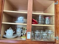 Cabinet view showing porcelain pieces on left shelves and glass storage pieces on right