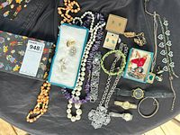All jewelry items laid out on black fabric including necklaces, bracelets, earrings, brooches, cufflinks, watches