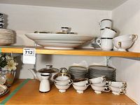 Overall view upper shelf showing large oval platter, cups, mugs, stacks of plates