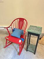 Rocking chair with pillow beside narrow green-top table