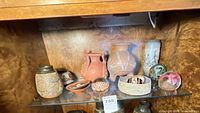 Front view of all pottery, stone bowl, paperweights on glass shelf