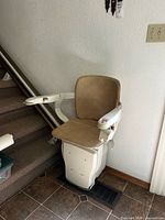 Stairlift chair at base of staircase showing seat, arms, footrest and control