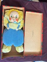 Doll in open box showing full body, clothing and interior of box