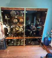 Front view of both burl veneer display cabinets showing glass doors, brass trim, interior glass shelves