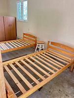 Two natural pine twin slatted bed frames and wooden stool in room