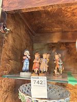 Group view of seven small porcelain figurines on glass shelf