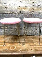 Both brass-tone metal vanity stools side by side on wooden surface