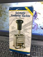 Front of boxed Pro Stamp Automatic Numbering Machine showing product and handle